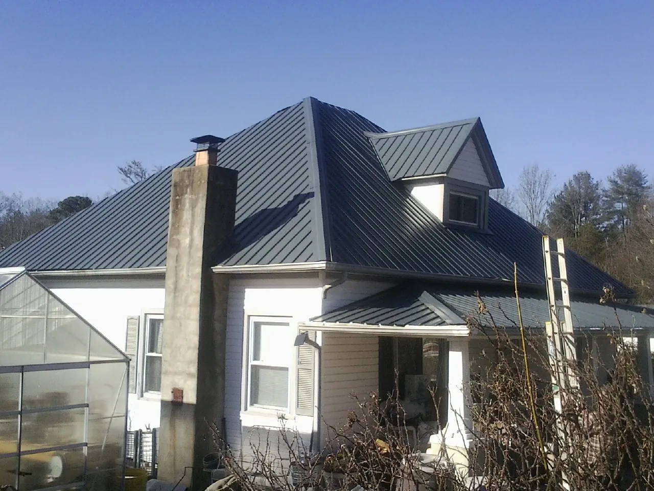 Dark blue standing seam metal roof on a white farmhouse with dormer — Slate & Tile Roof Repair by Roofing Brothers in Daisetta