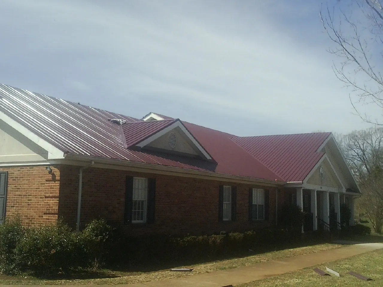 Red metal roof with gabled entries on a long brick building, from a Hail Damage Roof Repair job in Daisetta