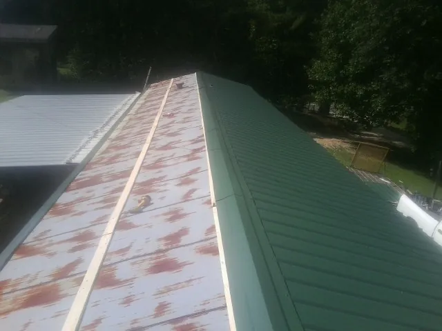 Old rusted panels beside newly installed green metal roofing — Wind Damage Roof Repair by Roofing Brothers in Daisetta