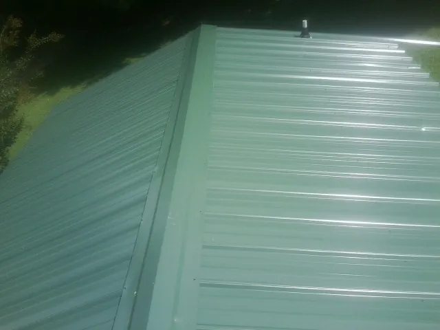 New green metal panels meeting at the ridge of a roof — Flat Roof Repair work by our crew in Daisetta