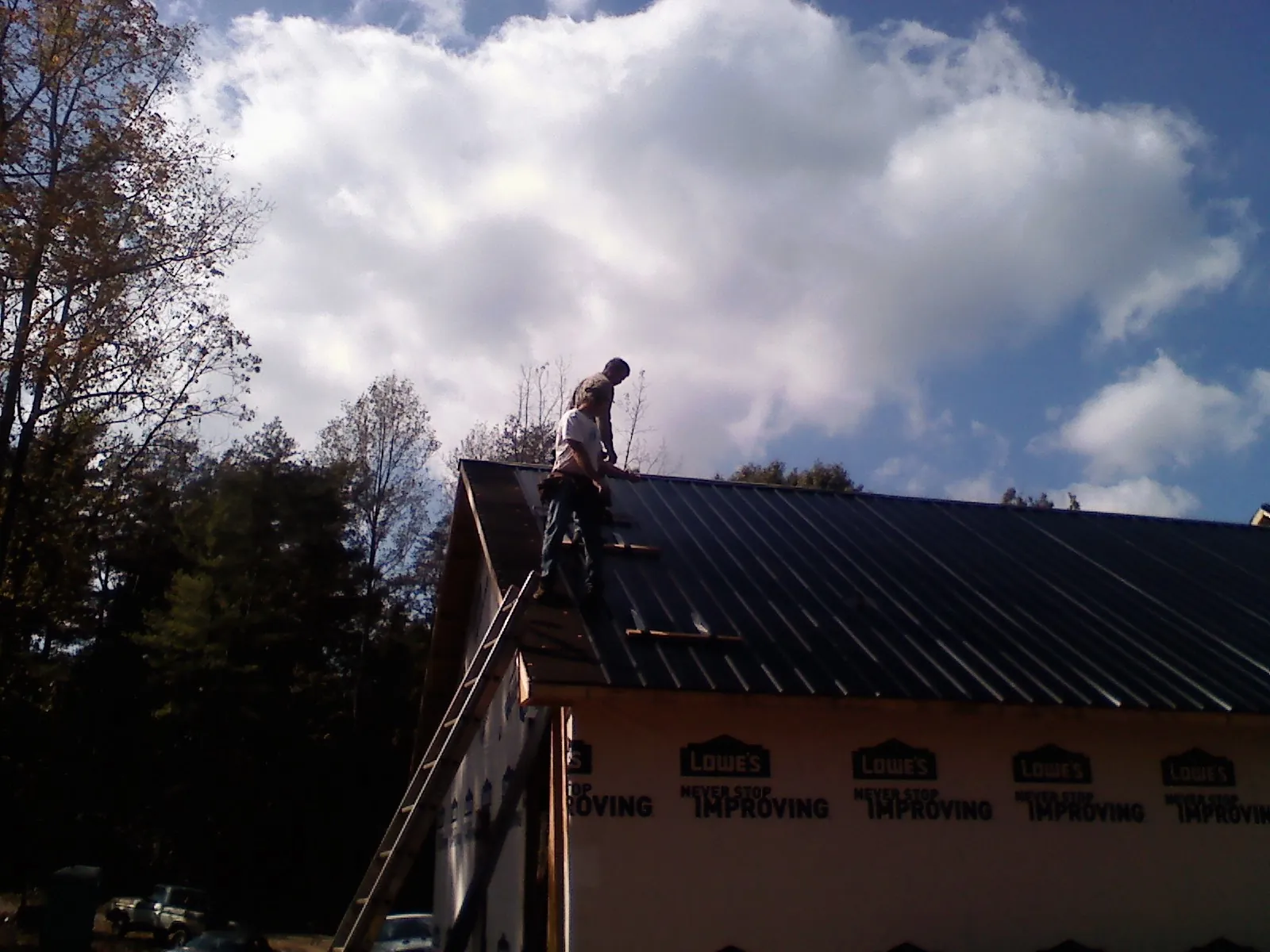 Roofer fastening dark metal panels high against a cloudy sky, from a Roof Inspection job in Daisetta