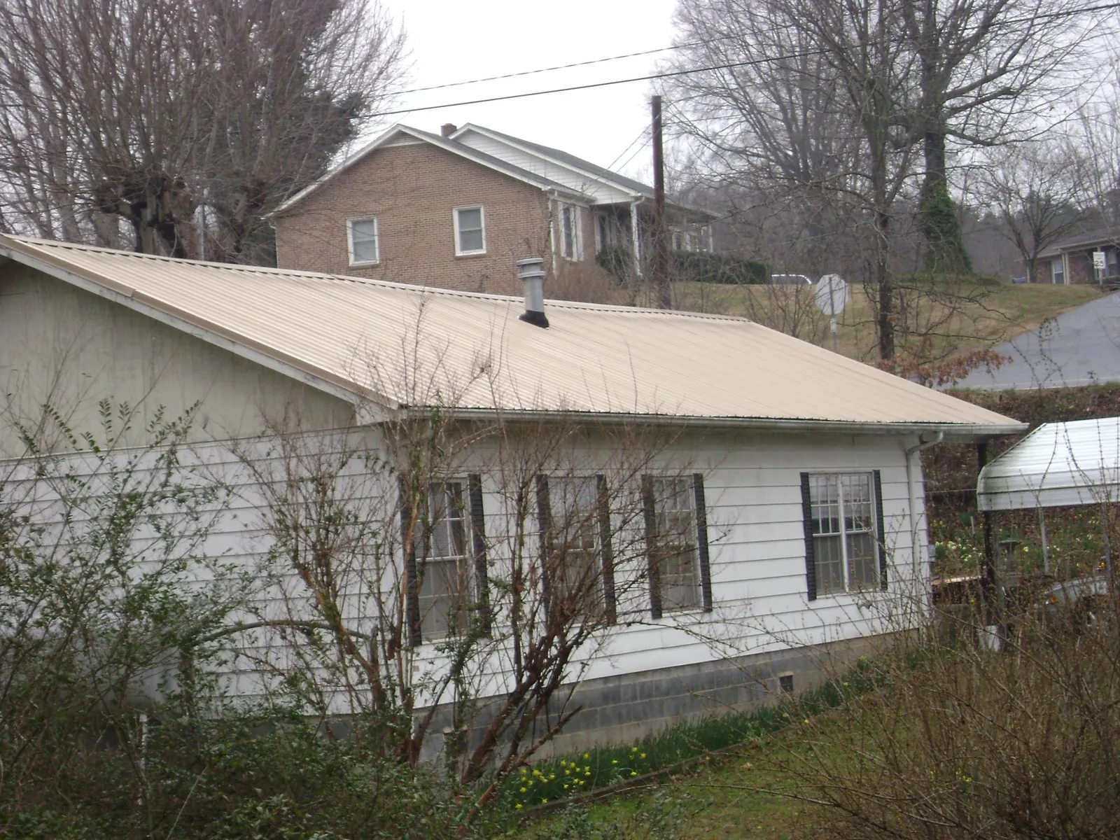 Tan metal roof on a white sided house set into a hillside — Commercial Roofing by Roofing Brothers in Daisetta