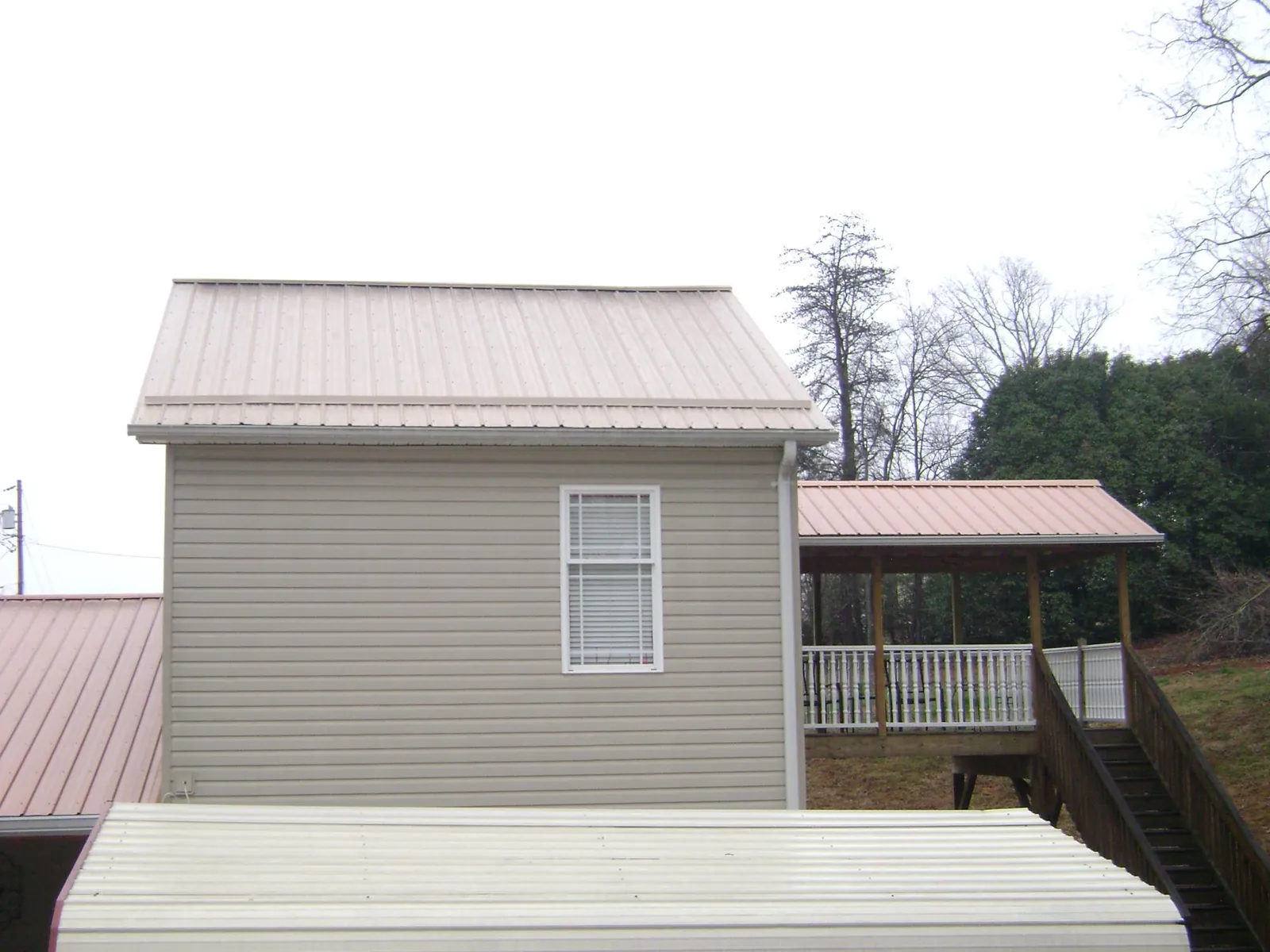 Tan metal roofs on a two story addition and attached porch, from a Roof Replacement job in Daisetta